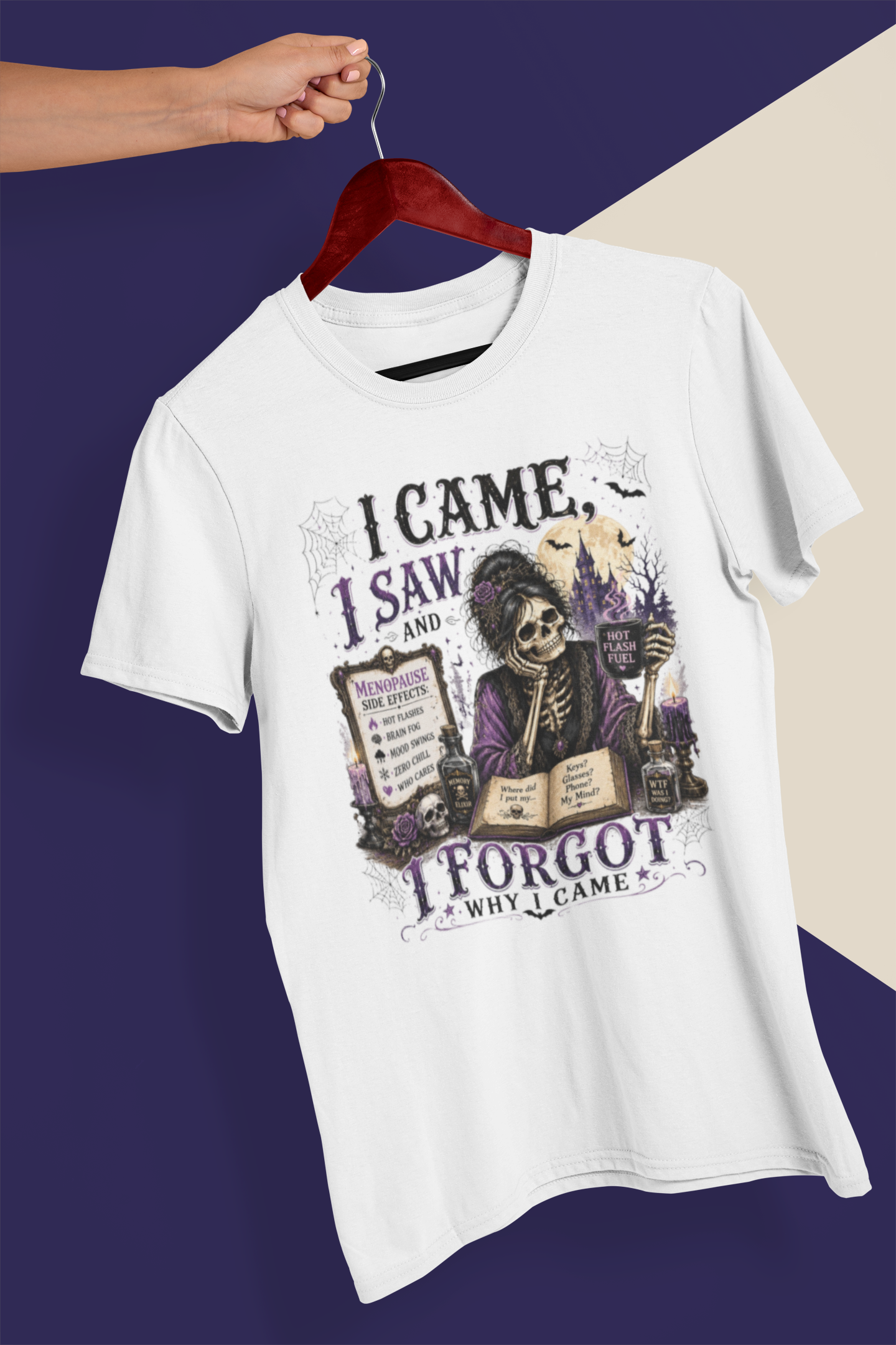 A white short-sleeve graphic T-shirt hanging on a dark red wooden hanger against a split purple and beige background. A human arm and hand are visible holding the hanger, which classifies the subject_type as Lifestyle under the schema rules.
