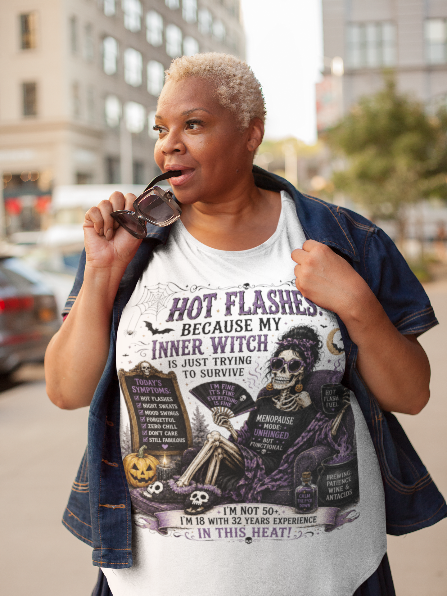 A woman wearing a white graphic t-shirt with a Halloween-themed design, styled with a dark blue denim jacket in an outdoor urban setting.